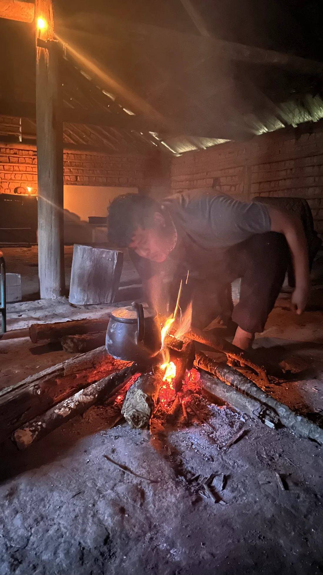 Homem atiça uma fogueira, com uma chaleira ao lado